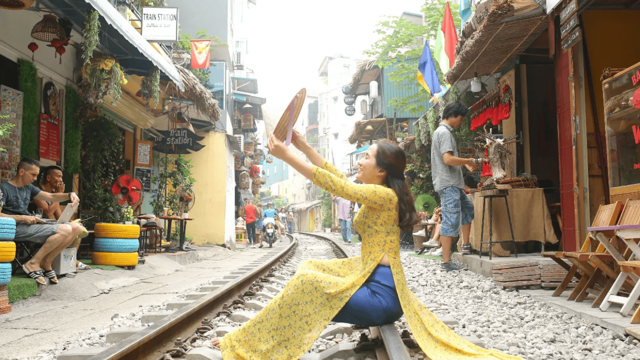 a woman wearing a yellow Ao Dai sitting on the tracks of Hanoi Unique Train Street