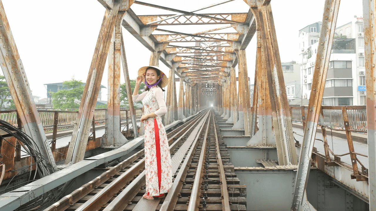 a woman wearing an Ao Dai standing on the tracks of Long Bien Bridge