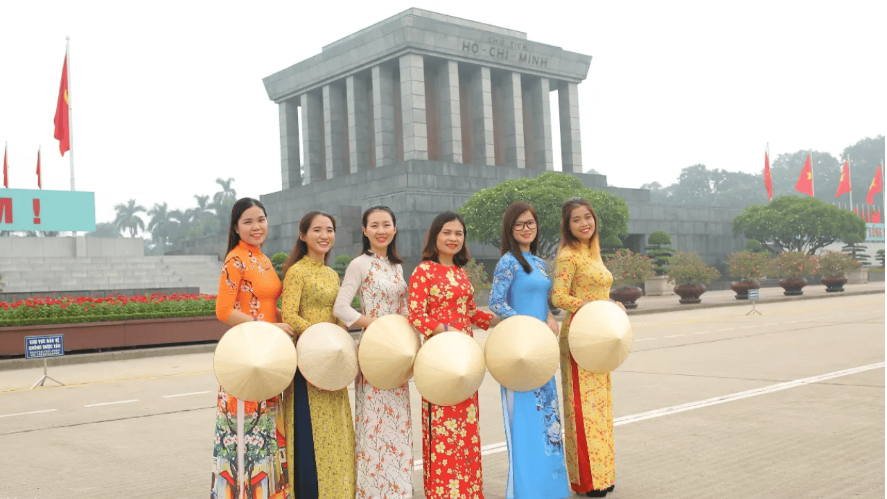 women wearing ao dais while carrying conical hats near the Ho Chi Minh Mausoleum